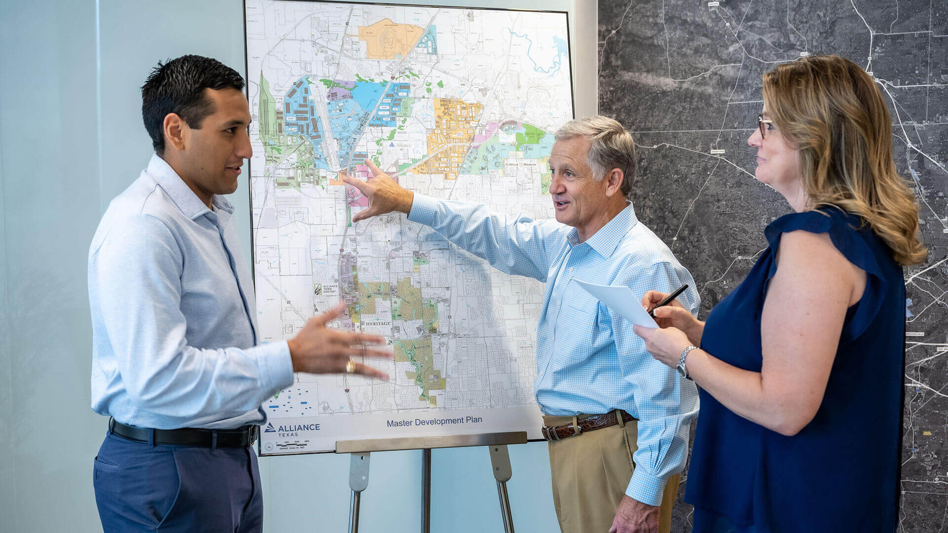 A man shows a master development map to two colleagues.