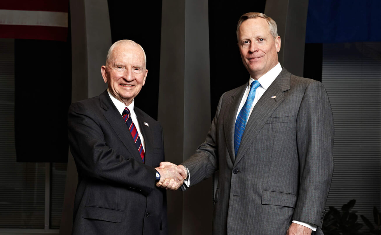 Ross Perot Sr. and Ross Perot Jr. shake hands. A text carousel overlay reads, ‘A legacy of commitment, strength, integrity’.