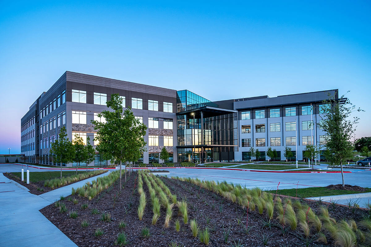 A four-story brick and glass building is fronted by new landscaping at AllianceTexas.