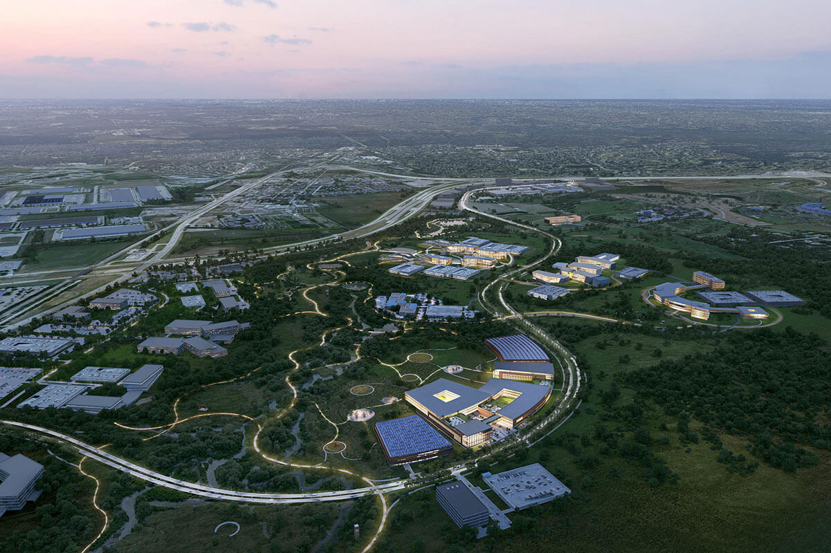 Roadways ring buildings, landscaping and waterways as seen from the air at sunset.