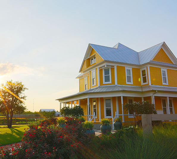 A yellow and white, two-story home is surrounded by green grass and trees in Denton County, Texas.