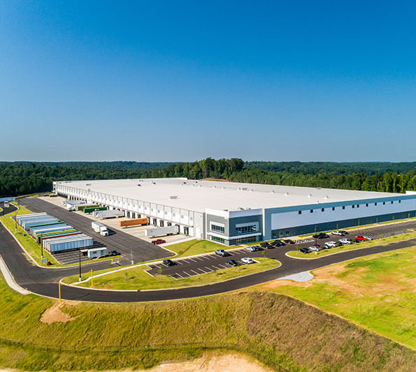 A low, white industrial building is seen from the air.